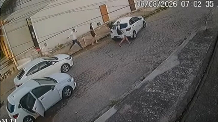 Homens descem de três carros brancos e correm por uma rua de paralelepípedos registrada por uma câmera de segurança