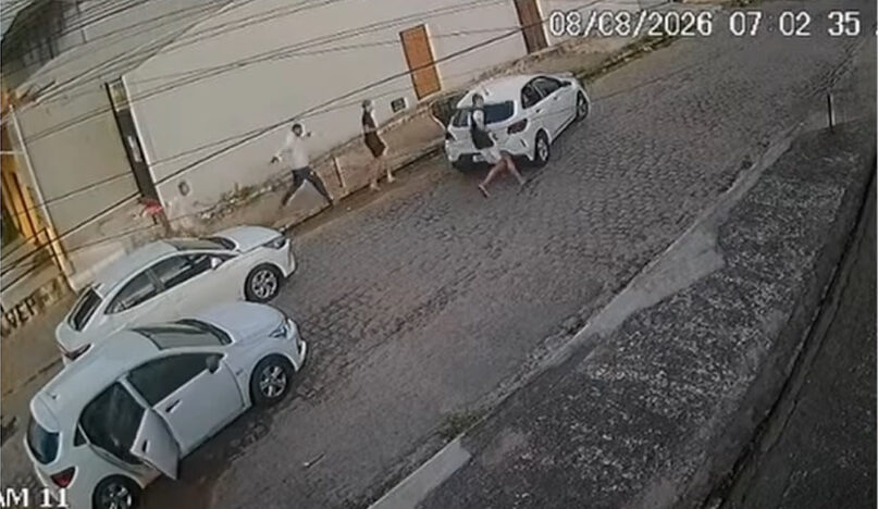 Homens descem de três carros brancos e correm por uma rua de paralelepípedos registrada por uma câmera de segurança