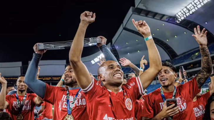Jogador do América ergue os braços durante comemoração de título ao lado de companheiros no gramado