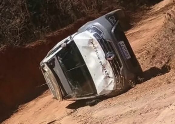 Viatura da Polícia Militar capotada em uma estrada sem pavimentação, próxima a uma área de vegetação