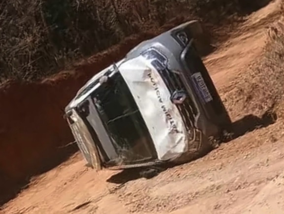 Viatura da Polícia Militar capotada em uma estrada sem pavimentação, próxima a uma área de vegetação