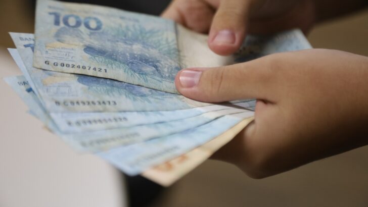 Pessoa segura e organiza várias cédulas de real, incluindo notas de R$ 100
