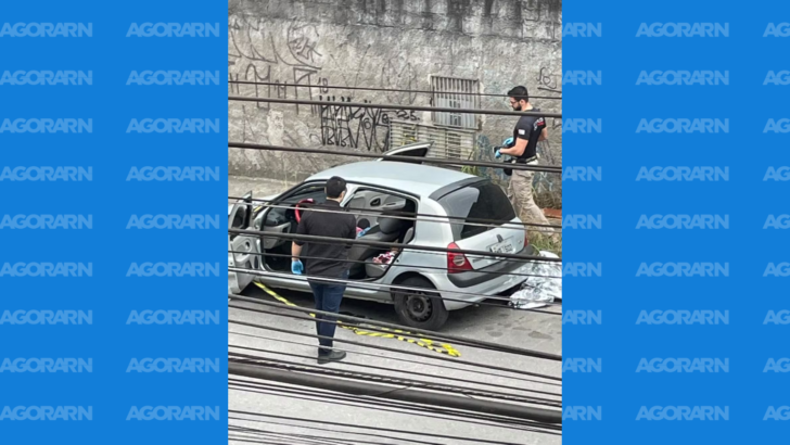 Dois peritos usando luvas examinam um carro prata estacionado e isolado por uma faixa de segurança em uma rua de São Paulo