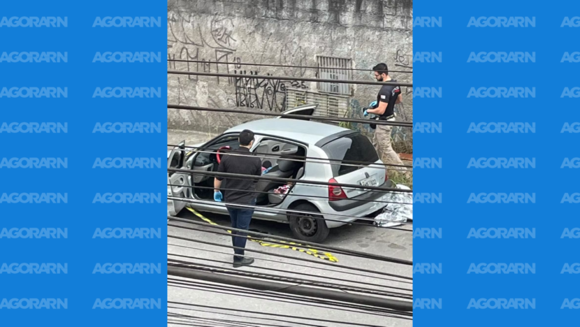 Dois peritos usando luvas examinam um carro prata estacionado e isolado por uma faixa de segurança em uma rua de São Paulo
