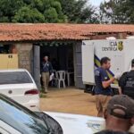Agentes da Polícia Civil e da perícia estão reunidos diante de um imóvel, ao lado de viaturas e de um veículo da Polícia Científica