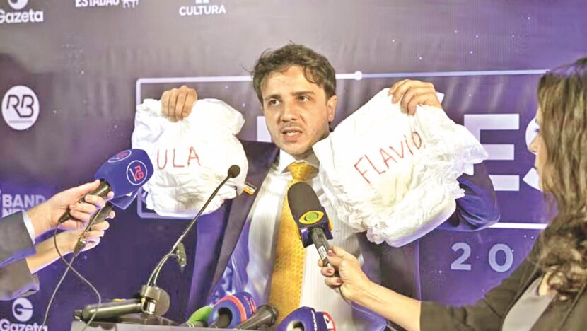 Renan Santos exibe fraldas com os nomes Lula e Flávio durante debate na Band