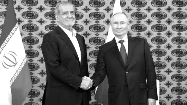 Vladimir Putin cumprimenta com aperto de mãos uma autoridade iraniana diante das bandeiras dos dois países, em foto em preto e branco