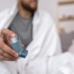 Homem segura um inalador para asma enquanto está sentado em uma cama