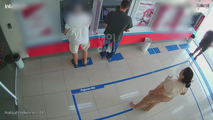 Imagem de câmera de segurança mostra pessoas diante de terminais de caixas eletrônicos em uma agência bancária