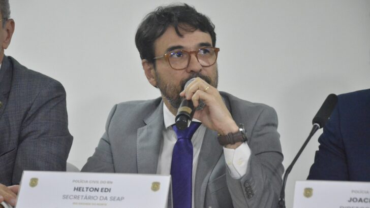 Helton Edi Xavier fala ao microfone sentado à mesa