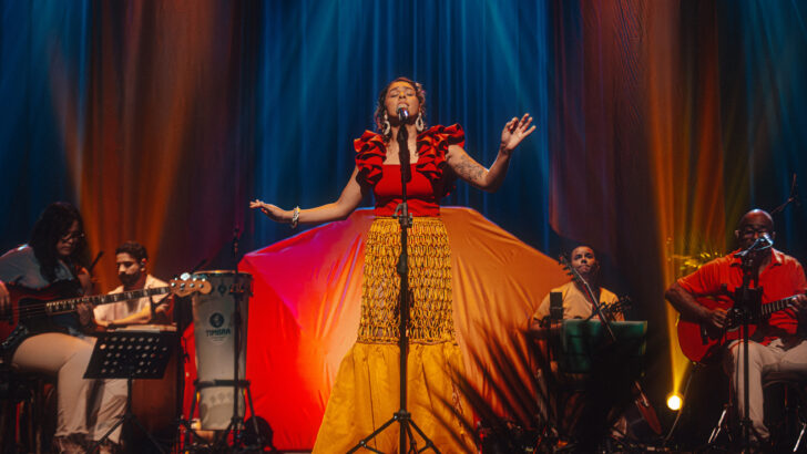Dani Cruz canta ao microfone acompanhada por músico no palco
