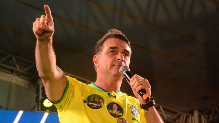 Flávio Bolsonaro fala ao microfone e aponta para o público durante ato político