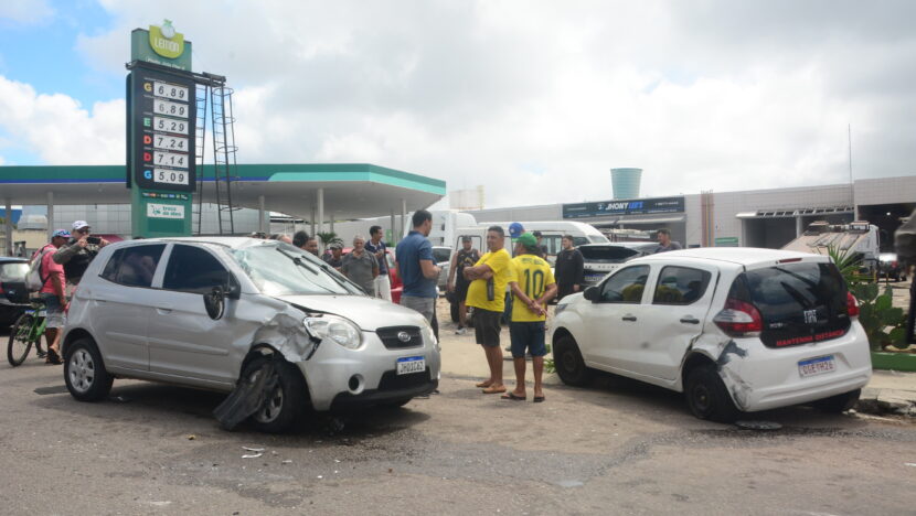 Dois carros com danos após acidente em frente a um posto de combustíveis, com pessoas reunidas próximas aos veículos