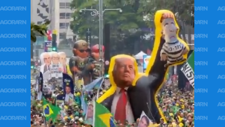 Boneco gigante de Donald Trump, de terno e gravata vermelha, ergue uma representação de Lula com roupa listrada de presidiário, acima de manifestantes e bandeiras do Brasil na Paulista.