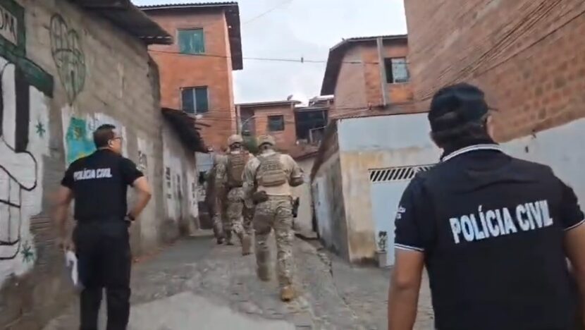 Policiais civis caminham por uma rua durante diligência policial