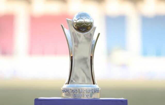 Troféu de competição de futebol sobre pedestal, com arquibancadas desfocadas ao fundo