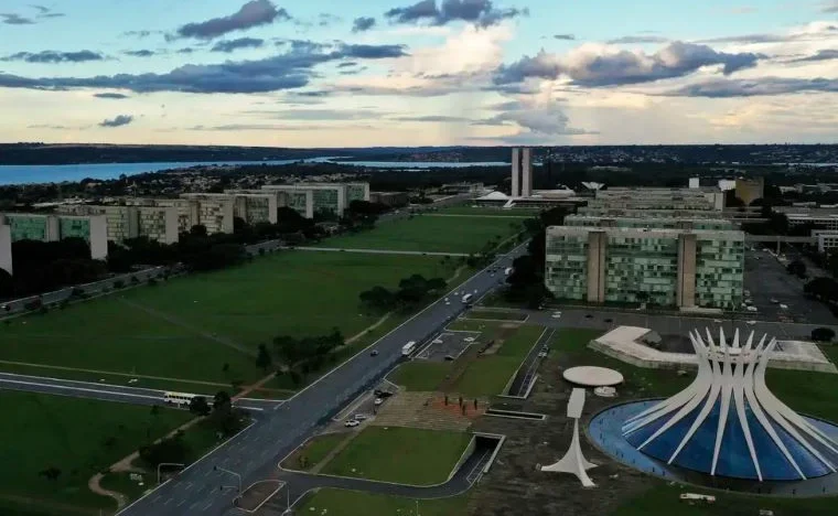 Vista aérea da Esplanada dos Ministérios, em Brasília, com prédios públicos e a Catedral Metropolitana em primeiro plano