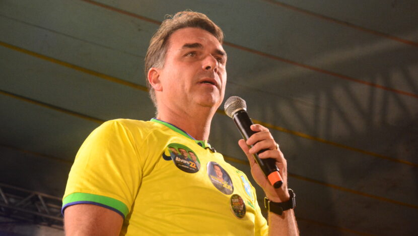 Homem de camisa amarela segura microfone durante ato político