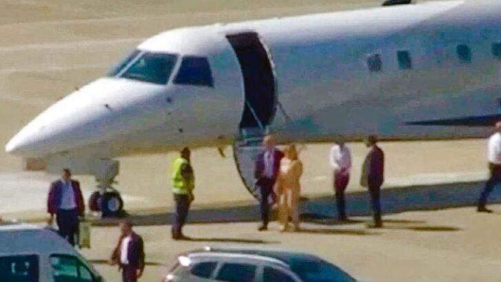 Jato executivo branco parado na pista de um aeroporto, com a porta aberta e um grupo de pessoas caminhando ao lado da aeronave