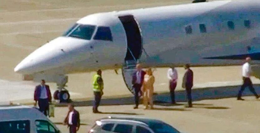 Jato executivo branco parado na pista de um aeroporto, com a porta aberta e um grupo de pessoas caminhando ao lado da aeronave