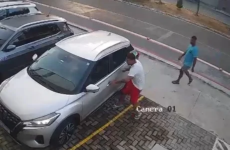 Imagem de câmera de segurança mostra uma pessoa junto à porta de um carro estacionado e outras pessoas nas proximidades