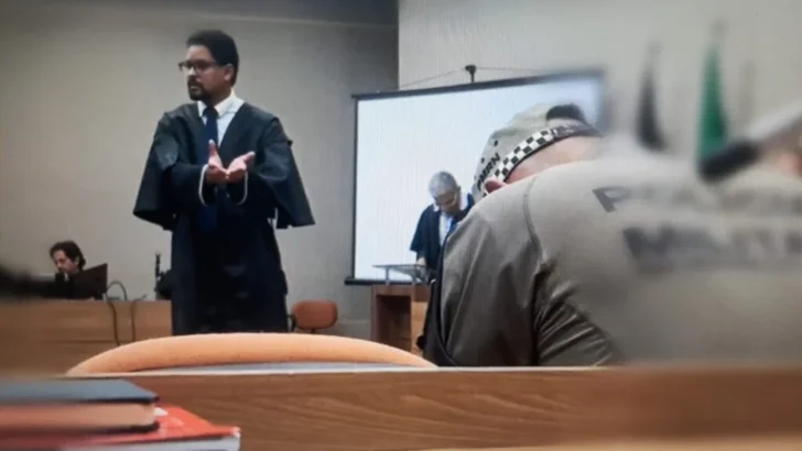 Homem de beca fala em plenário durante julgamento no Tribunal do Júri, enquanto outra pessoa permanece sentada