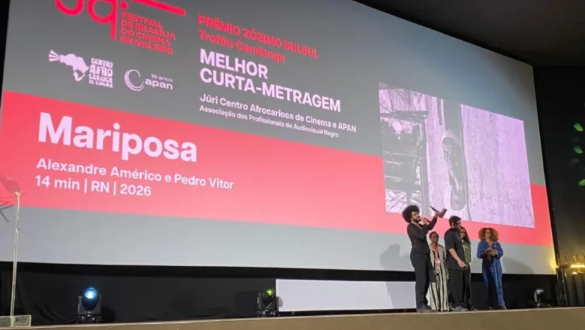 Tela de cerimônia do Festival de Brasília exibe o anúncio de “Mariposa” como vencedor do Prêmio Zózimo Bulbul de Melhor Curta, com pessoas no palco