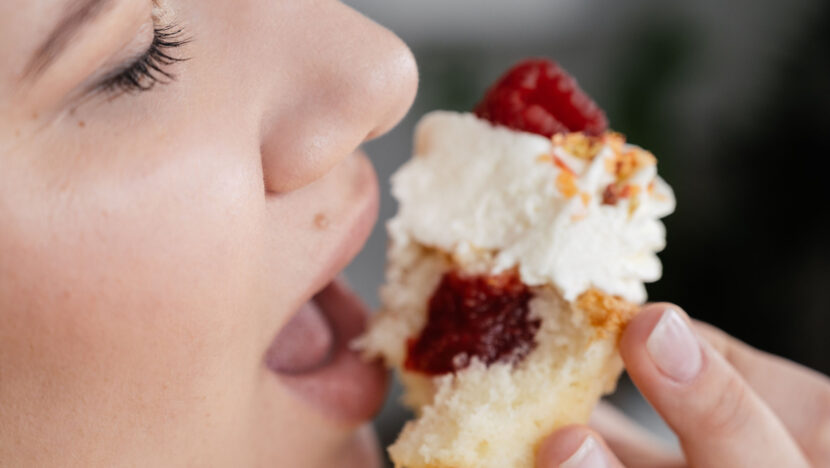 Mulher leva à boca um doce com chantili e geleia de frutas vermelhas