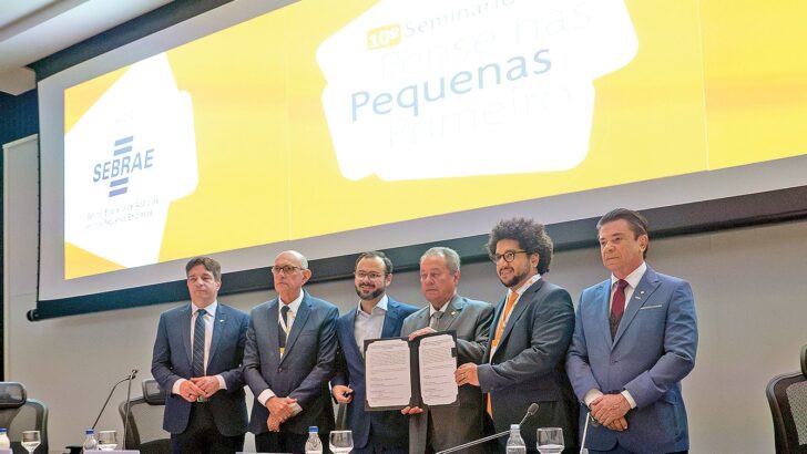 Cinco homens de terno em pé no palco, diante de um telão amarelo com a palavra Pequenas e a marca do Sebrae