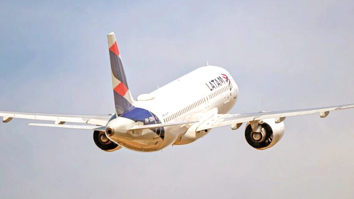 Avião da Latam durante decolagem, com trem de pouso recolhendo, sob céu claro