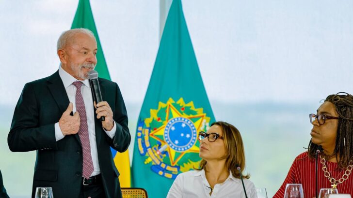 Presidente Lula fala ao microfone diante das bandeiras oficiais da Presidência