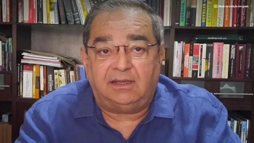 Álvaro Dias, de camisa azul e óculos, fala em transmissão ao vivo diante de uma estante de livros
