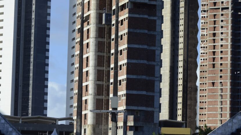 Prédios altos em construção, com estrutura de concreto e paredes de tijolos aparentes, ao lado de edifícios já concluídos