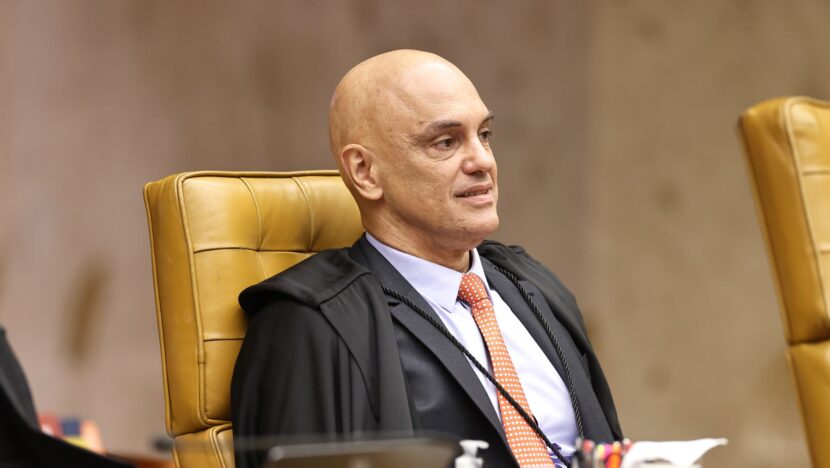 Homem calvo de toga preta e gravata laranja sentado em cadeira amarela no plenário do STF