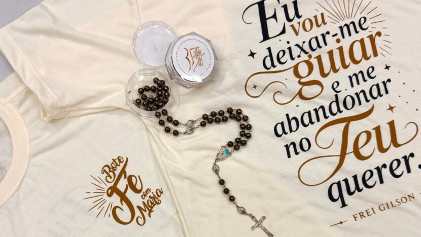Camisetas cor creme com frase de Frei Gilson e o logotipo do Bote Fé, ao lado de um terço marrom e sua caixinha