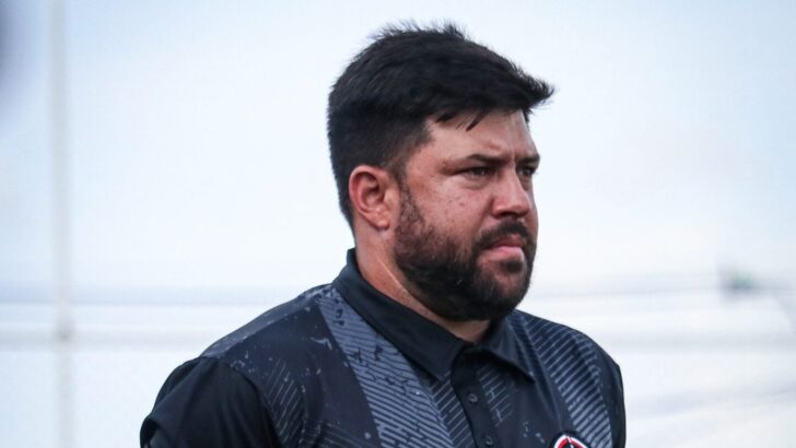Técnico Daniel Rocha, de barba e camisa polo preta, observa à beira do campo