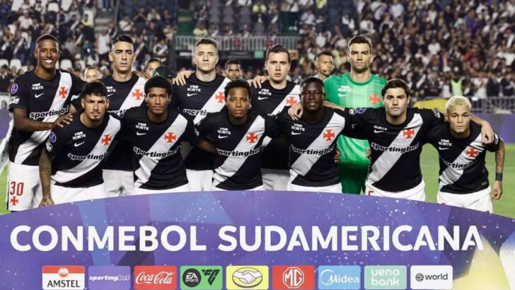 Jogadores do Vasco de uniforme preto posam para foto oficial em campo, atrás de faixa da Conmebol Sul-Americana