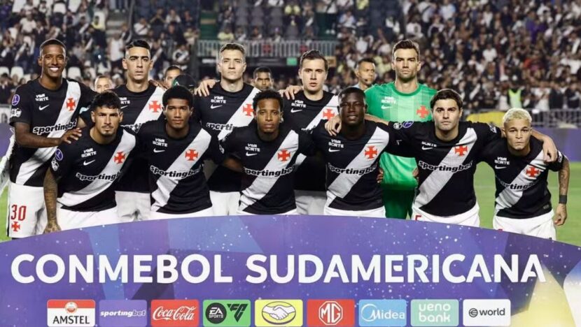 Jogadores do Vasco de uniforme preto posam para foto oficial em campo, atrás de faixa da Conmebol Sul-Americana
