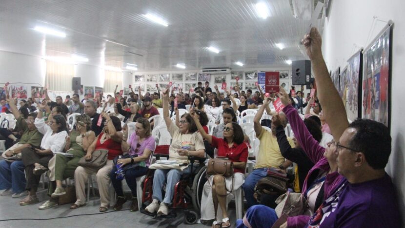 Plateia lotada em assembleia de professores, com pessoas de braços erguidos votando