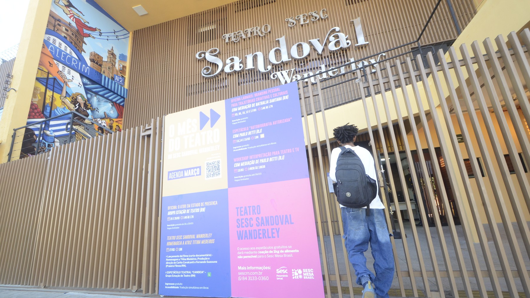 Entrada do teatro com letreiro do nome da casa, painéis coloridos e grade de madeira