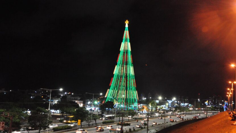 Árvore de Natal gigante iluminada em verde à noite, às margens de avenida movimentada
