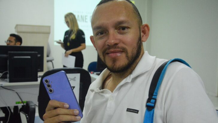 Homem sorri segurando um celular recuperado em sala da Polícia Civil