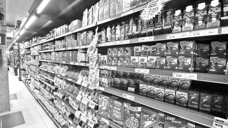 Corredor de supermercado com prateleiras cheias de produtos industrializados, em preto e branco