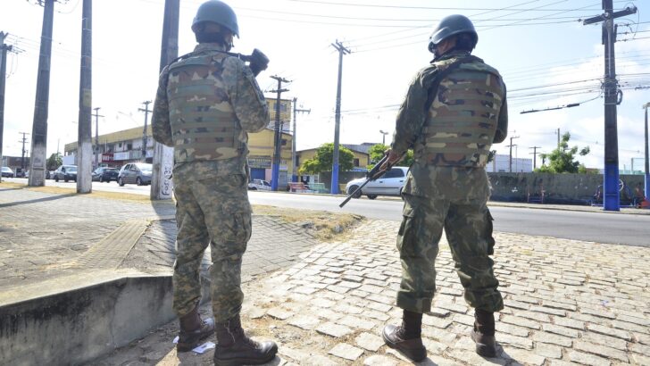 Dois agentes fardados, de capacete e colete, em pé numa rua, de costas para a câmera