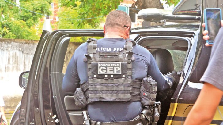 Policial penal de colete tático entra em viatura, de costas, com a palavra GEP escrita nas costas do colete