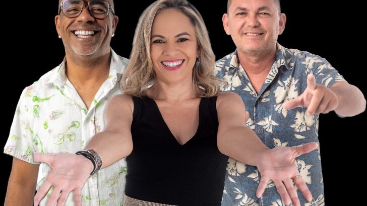 Três integrantes da banda sorriem com os braços estendidos à frente, em foto de estúdio sobre fundo escuro