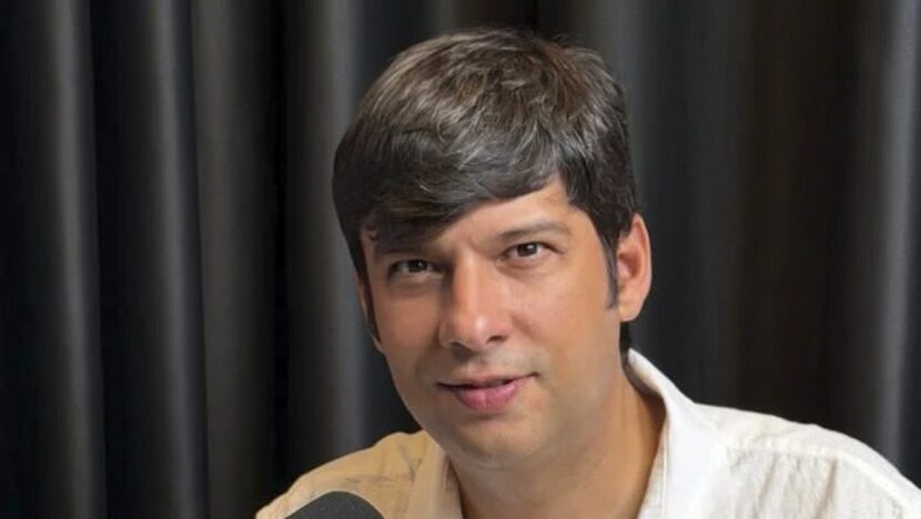 Homem de camisa clara diante de um microfone de estúdio, durante entrevista