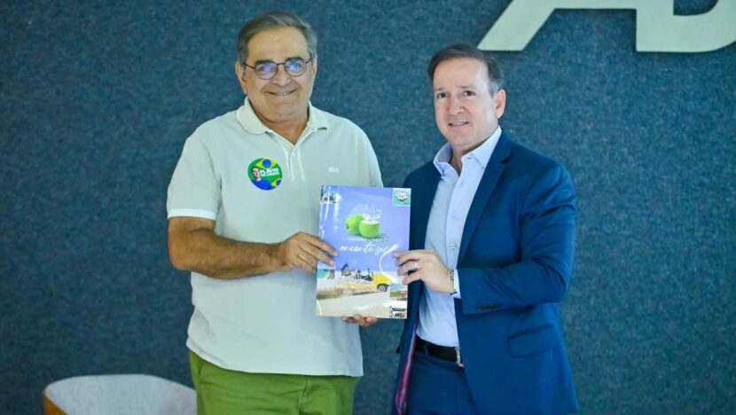 Dois homens em pé diante do letreiro da ABIH segurando juntos um exemplar impresso da Agenda da Hotelaria Potiguar