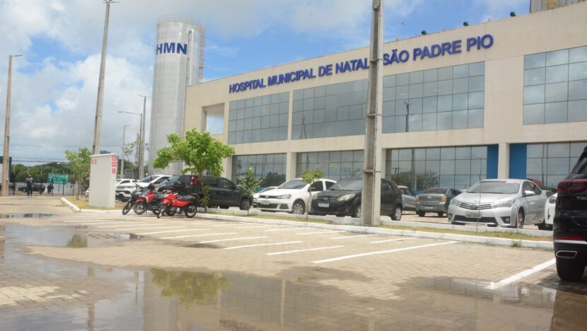 Fachada do Hospital Municipal de Natal com o letreiro São Padre Pio sobre a entrada e carros estacionados em frente