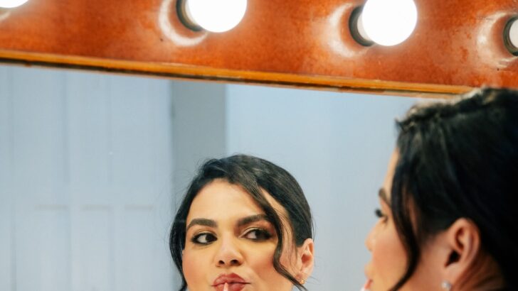 A comediante Morgana Camila observa o próprio reflexo em espelho de camarim cercado por lâmpadas